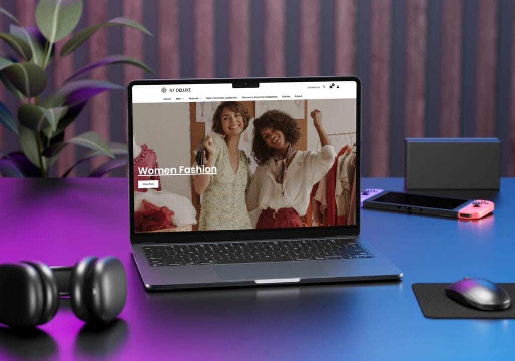 A stylish workspace features a laptop with a women's fashion website on screen, showing two smiling women dressed in trendy attire. Surrounding items include a plant, a tablet, a smartphone, headphones, and a game controller, all on a gradient pink and purple surface.